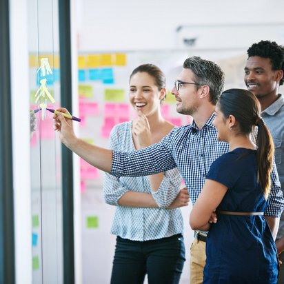 Teamwork und Ideensammlung im kreativen Workshop. Team steht vor einem Whiteboard und entwickelt gemeinsam kreative Ideen.