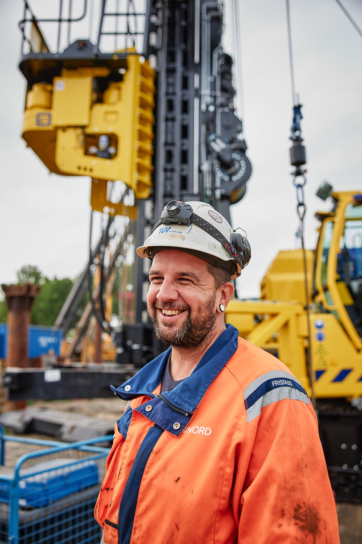 Lächelnder TÜV NORD-Mitarbeiter mit Schutzhelm und Warnkleidung auf einer Baustelle.