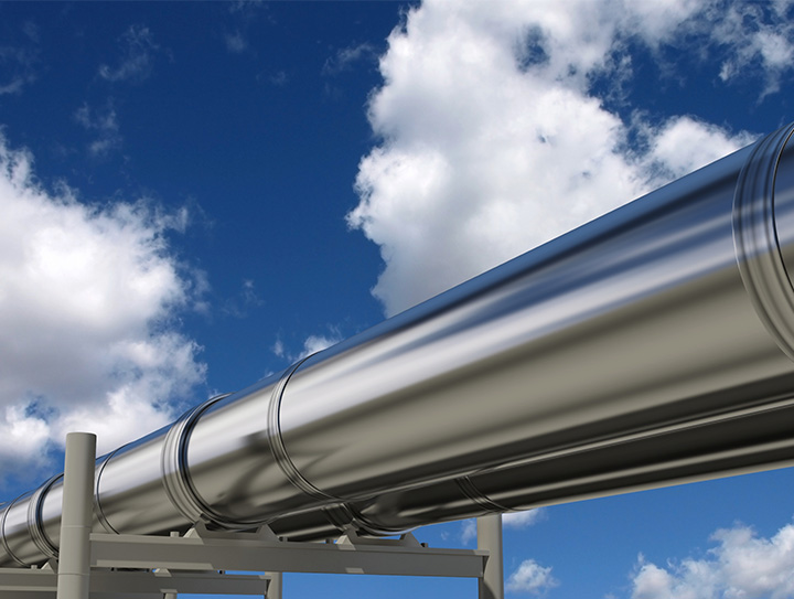 Im Vordergrund zu sehen ist eine silbern glänzende Pipeline, im Hintergrund blauer Himmel mit wenigen weißen Wolken.