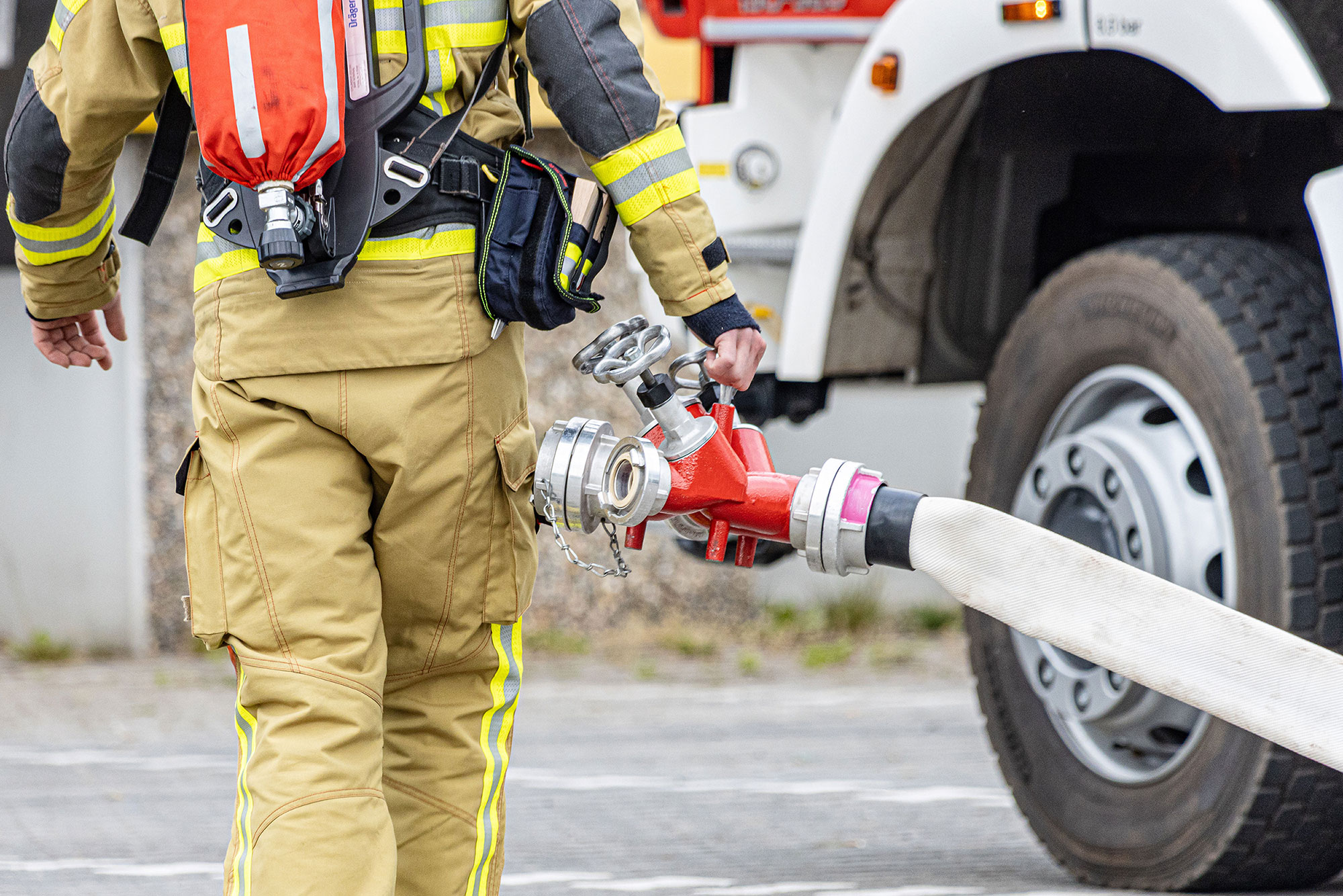 Feuerwehrmann mit Schlauch vor einem Feuerwehrauto