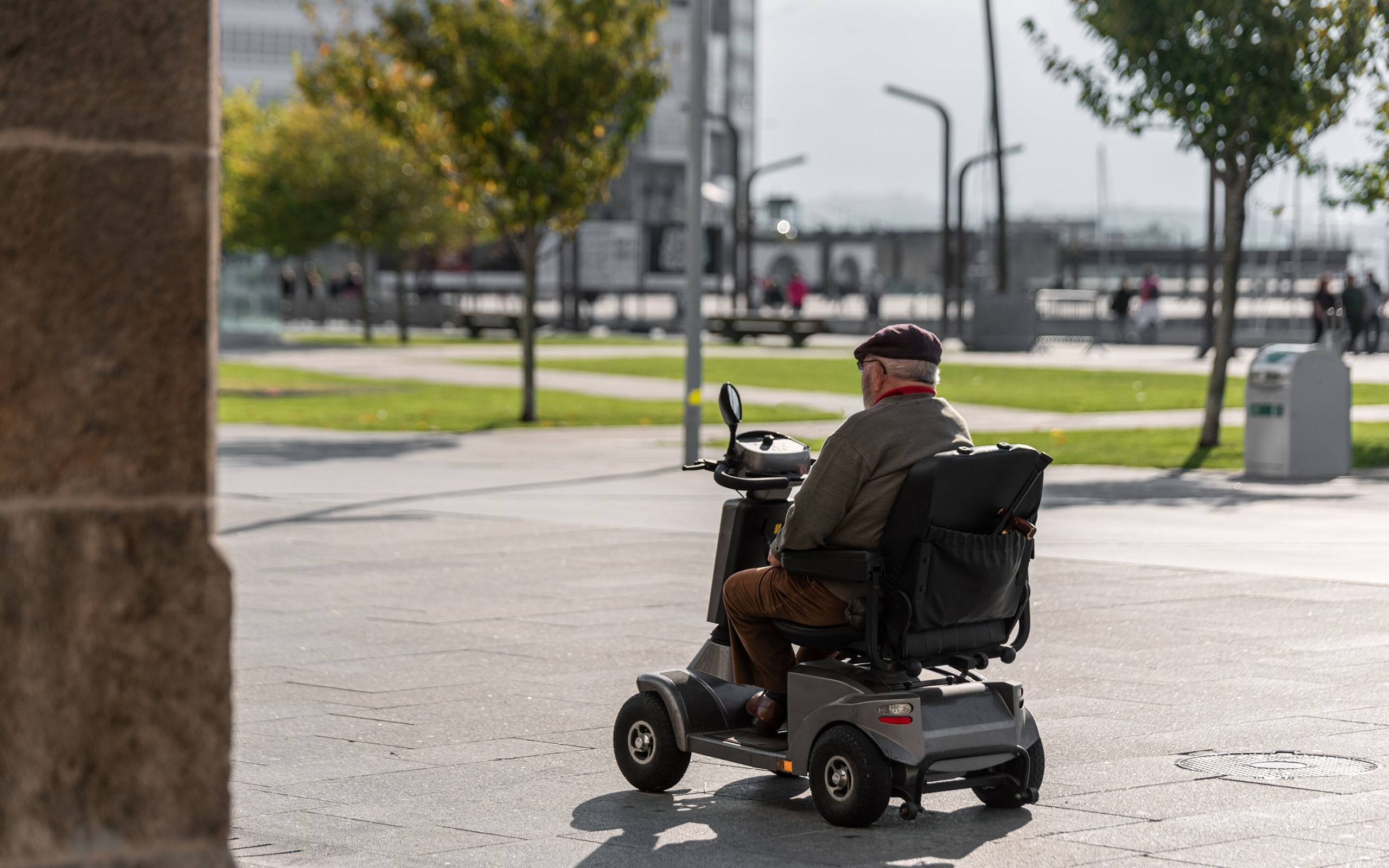 Älterer Mann fährt mit einem Elektrorollstuhl über einen sonnigen Platz in der Stadt