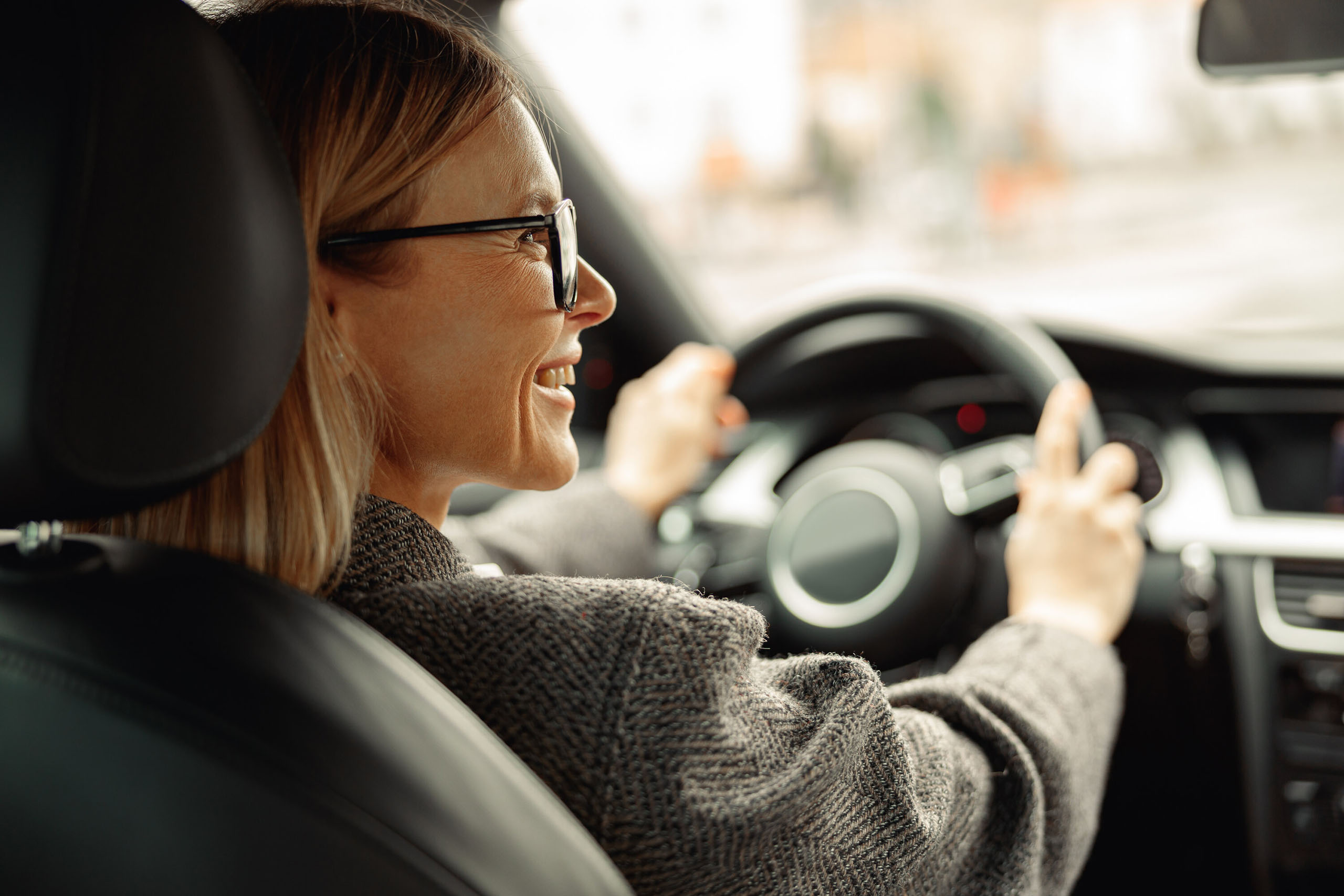 Lächelnde Frau fährt ein Auto und hält das Lenkrad mit beiden Händen