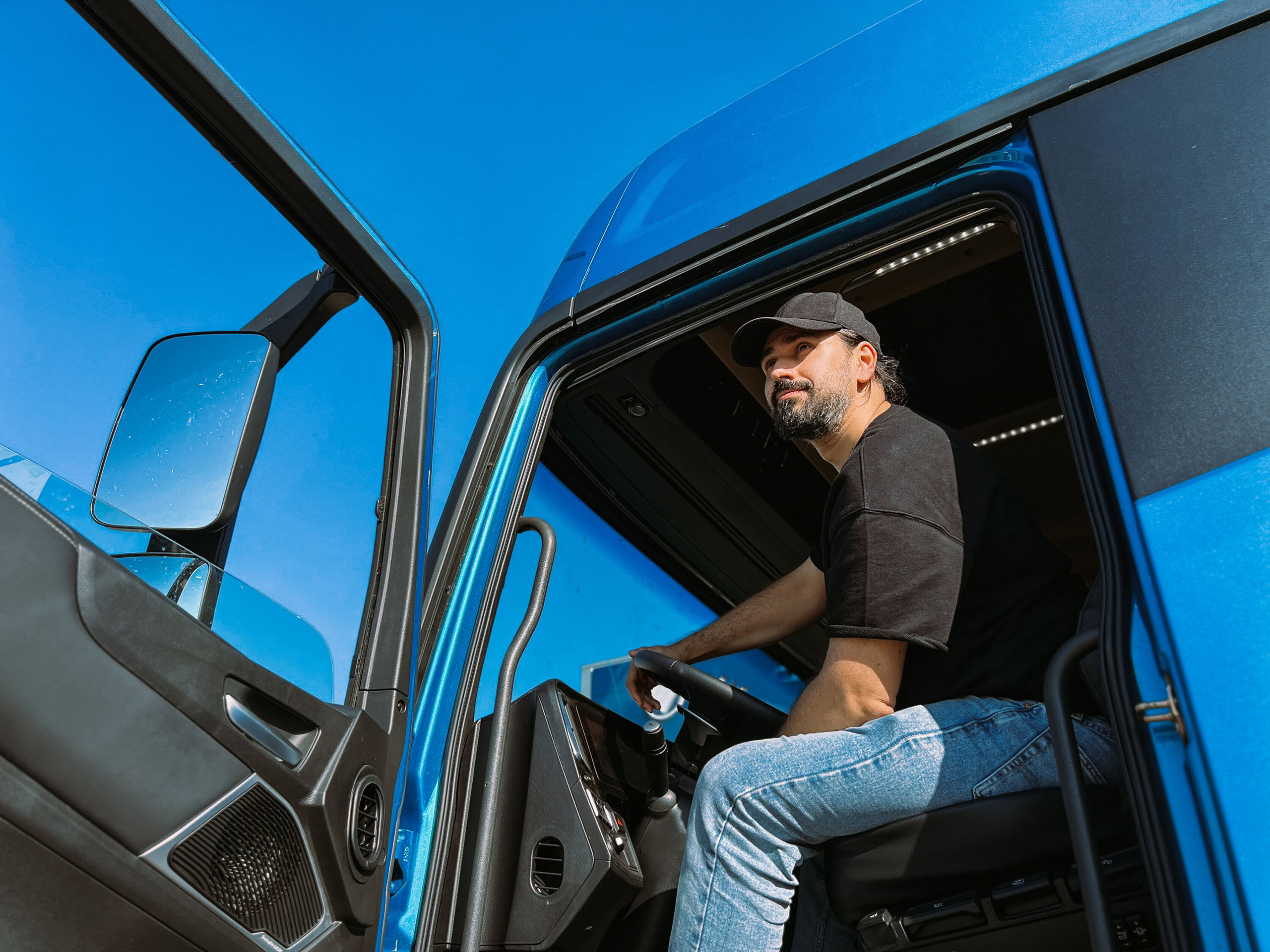 Lkw-Fahrer mit Basecap sitzt in einem blauen Lkw und blickt aus der geöffneten Tür