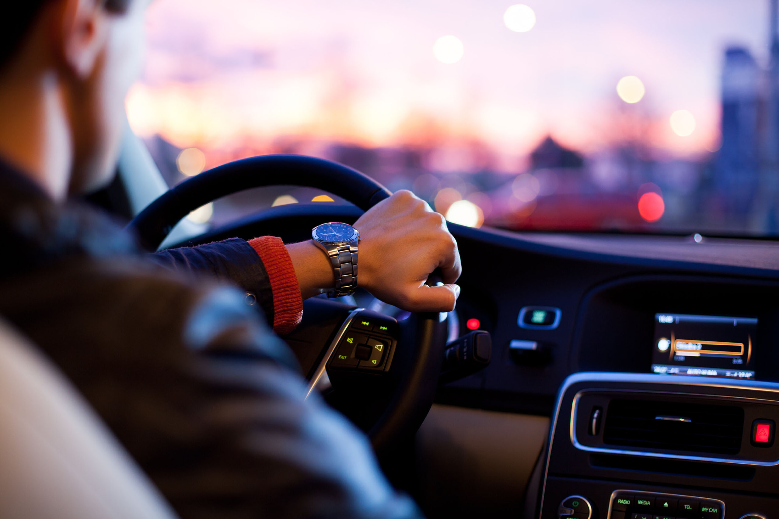 Person mit Lederjacke fährt ein Auto bei Sonnenuntergang durch die Stadt