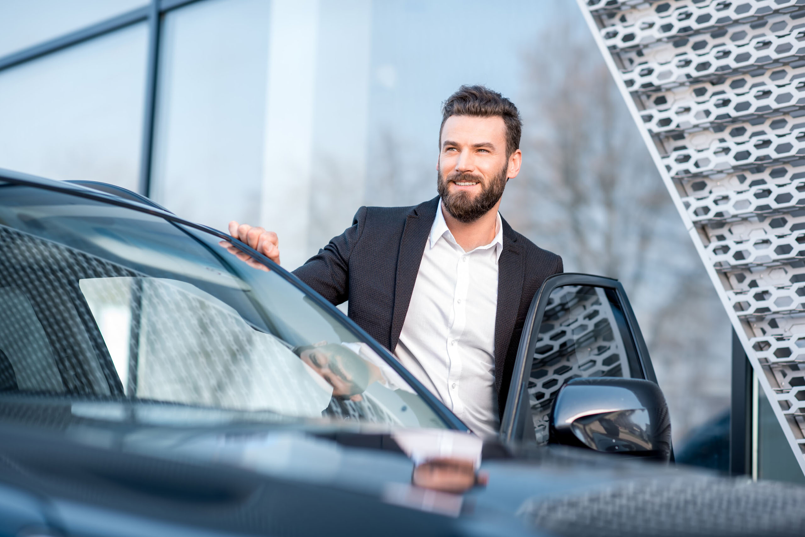 Mann im Anzug steigt lächelnd aus einem schwarzen Auto vor einem modernen Gebäude