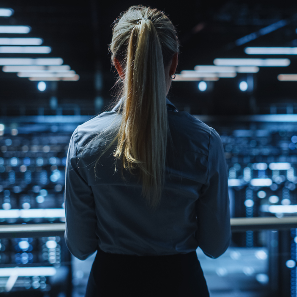 Eine Frau steht in einem dunklen Raum voller Computer mit dem Rücken zum Betrachter.