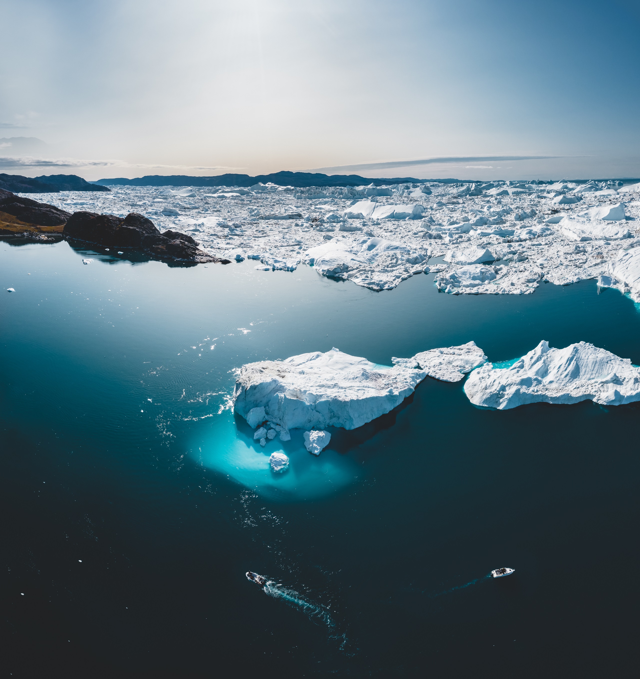 Luftaufnahme von schmelzenden Eisbergen in der Arktis mit zwei Booten im Wasser