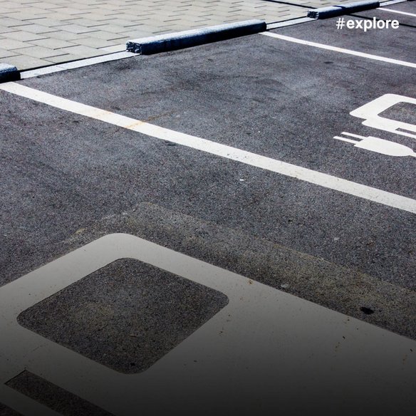 Speziell gekennzeichnete Parkplätze für Elektrofahrzeuge mit weißen Markierungen auf dunklem Asphalt. Die Stellplätze sind mit Elektroauto-Symbolen markiert und durch weiße Linien voneinander abgegrenzt.