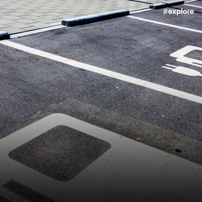 Speziell gekennzeichnete Parkplätze für Elektrofahrzeuge mit weißen Markierungen auf dunklem Asphalt. Die Stellplätze sind mit Elektroauto-Symbolen markiert und durch weiße Linien voneinander abgegrenzt.