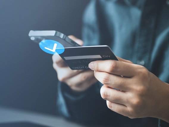 Person hält Smartphone und Kreditkarte für eine sichere Online-Zahlung in der Hand.