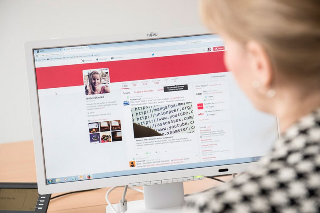 Ein Fujitsu-Computerbildschirm zeigt eine Social-Media-Profilseite mit rotem Banner. Im Vordergrund ist unscharf der Hinterkopf einer Person mit schwarz-weißem Muster auf der Kleidung erkennbar. Bild 3: Eine Treppe mit rotem Belag und Metallgeländer führt an einer großen Glaswand mit bunten politischen Motiven und Darstellungen vorbei. Unten auf der Treppe sind zwei Personen zu sehen. Bild 4: Eine Person in rotem Mantel und grünem Schal geht vor einem großen, repräsentativen Gebäude mit klassischer Fassade und modernen Anbauten über einen Platz. Weitere Menschen sind im Hintergrund zu sehen. Bild 5: Panoramablick auf eine Hafenstadt bei Dämmerung mit beleuchteten Hafenkränen links, einem markanten Gebäude mit wellenförmigem Dach in der Mitte und einer Stadtsilhouette mit Lichterreflexionen im Wasser.WiederholenClaude kann Fehler machen. Bitte überprüfen Sie die Antworten.