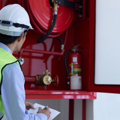 Sicherheitsprüfer inspiziert Wandhydrantenanlage und macht Notizen auf einem Klemmbrett.