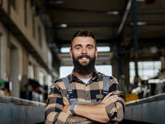 Person in Arbeitskleidung steht mit verschränkten Armen in einer Produktionshalle vor einer industriellen Anlage.