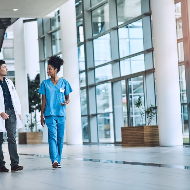 Zwei medizinische Fachkräfte gehen durch ein modernes Krankenhaus und unterhalten sich