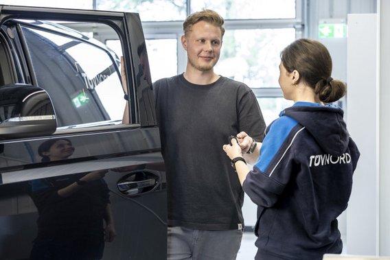 Kunde im Gespräch mit TÜV NORD Mitarbeiterin neben einem Fahrzeug