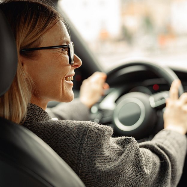 Lächelnde Frau fährt ein Auto und hält das Lenkrad mit beiden Händen