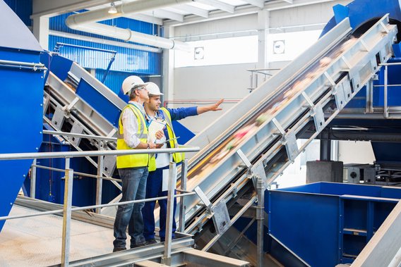 Zwei Personen besichtigen eine Recyclinganlage zur Abfallwirtschaft