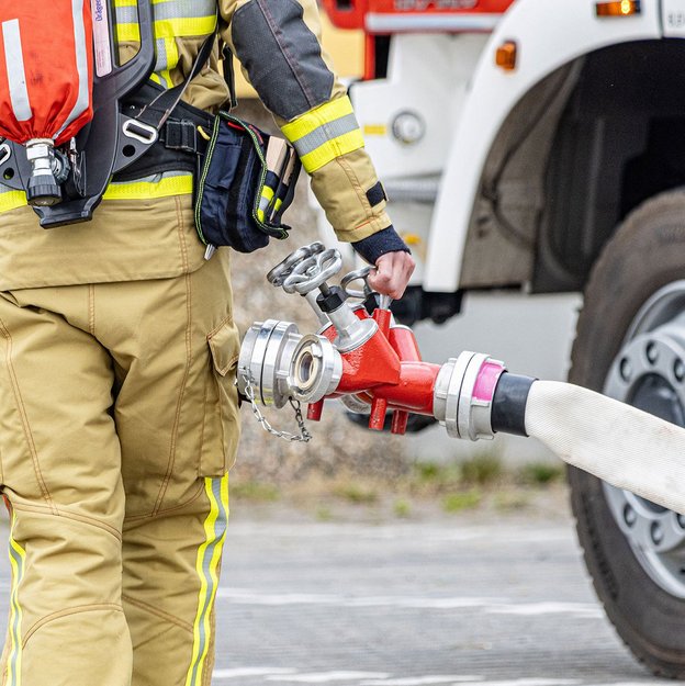 Feuerwehrmann mit Schlauch vor einem Feuerwehrauto