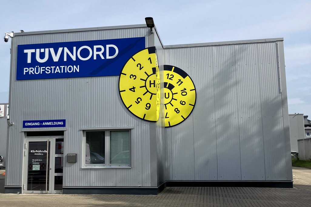 Frontansicht der TÜV NORD Station Wunstorf mit Hallentor und großer HU-Plakette an der Gebäudefassade.