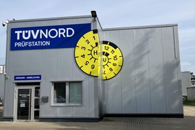 Frontansicht der TÜV NORD Station Wunstorf mit Hallentor und großer HU-Plakette an der Gebäudefassade.
