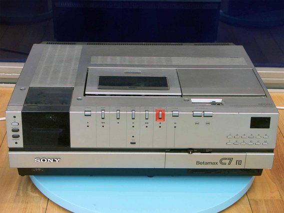 Ein Sony Betamax C7 Videorekorder aus den 1980ern in silber-grauer Farbe. Das Gerät hat zahlreiche Bedienknöpfe und ein Kassettenfach an der Front.