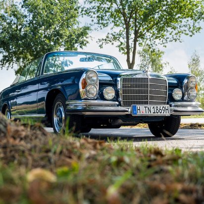 Blauer Oldtimer auf einer Straße mit Bäumen am Rand