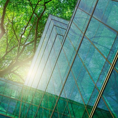 Moderne Glasgebäude mit Spiegelung von Bäumen im Sonnenlicht.