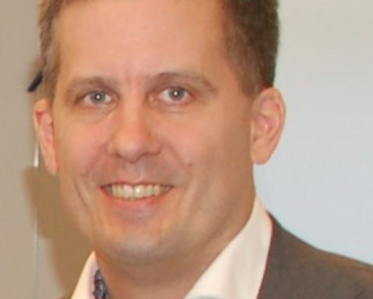 Porträt von Detlef Beltz in grauem Anzug und weißem Hemd vor hellem Hintergrund.