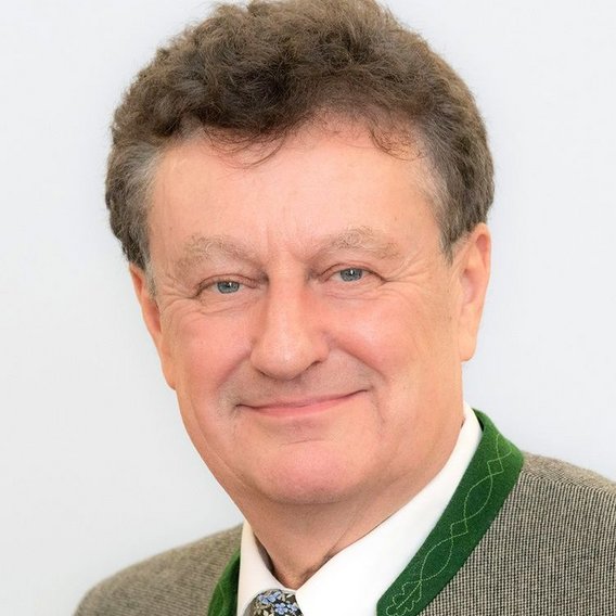 Ein Porträtfoto von Wolfgang M. Heckl vor weißem Hintergrund. Er trägt traditionelle bayerische Kleidung mit einer graugrünen Jacke mit grünem Revers, einem weißen Hemd und einer gemusterten Krawatte. Er hat welliges braungraues Haar und lächelt freundlich in die Kamera.