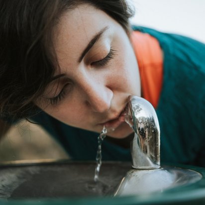Frau trinkt aus einem Trinkwasserspender