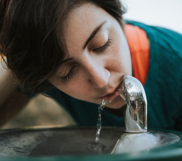 Frau trinkt aus einem Trinkwasserspender