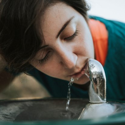 Frau trinkt aus einem Trinkwasserspender