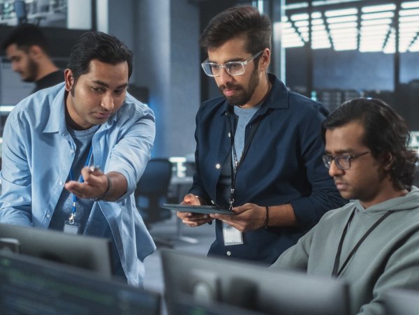 Gruppe von Personen arbeitet in einem modernen Büro mit Computern und Bildschirmen.