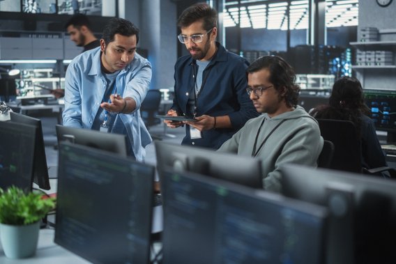 Gruppe von Personen arbeitet in einem modernen Büro mit Computern und Bildschirmen.