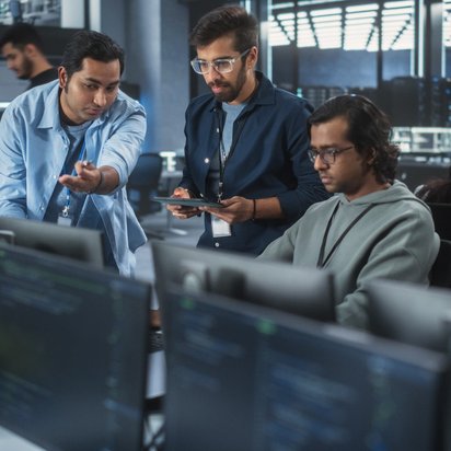 Gruppe von Personen arbeitet in einem modernen Büro mit Computern und Bildschirmen.