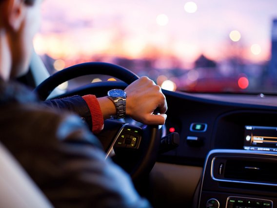 Person mit Lederjacke fährt ein Auto bei Sonnenuntergang durch die Stadt