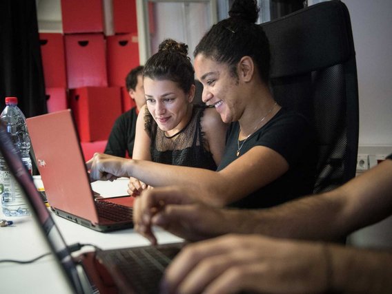 Zwei Frauen betrachten gemeinsam einen Laptop-Bildschirm und wirken engagiert und zufrieden mit ihrer Arbeit.