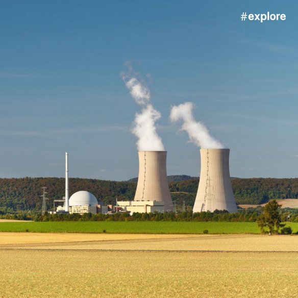 Ein Feld an einem wolkenlosen Tag. In der Ferne steht ein Kernkraftwerk. Aus den zwei Kühltürmen tritt Rauch aus.