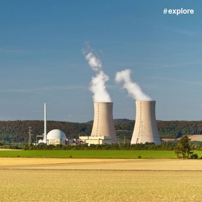 Ein Feld an einem wolkenlosen Tag. In der Ferne steht ein Kernkraftwerk. Aus den zwei Kühltürmen tritt Rauch aus.