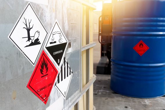 Container und Fass mit Gefahrgutkennzeichnungen für umweltgefährdende, korrosive und entzündbare Stoffe.