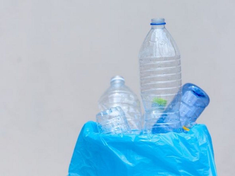 Mehrere leere Plastikwasserflaschen auf einer blauen Plastiktüte vor einem neutralen Hintergrund.