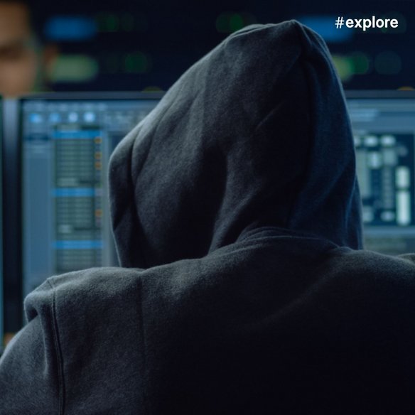  Eine Person in einem dunklen Kapuzenpullover sitzt vor mehreren Computerbildschirmen mit komplexen Datenvisualisierungen und Code-Interfaces.