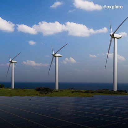 Eine Kombination aus erneuerbaren Energien: Solarmodule im Vordergrund und drei Windkraftanlagen auf grünen Feldern mit Meeresblick im Hintergrund.