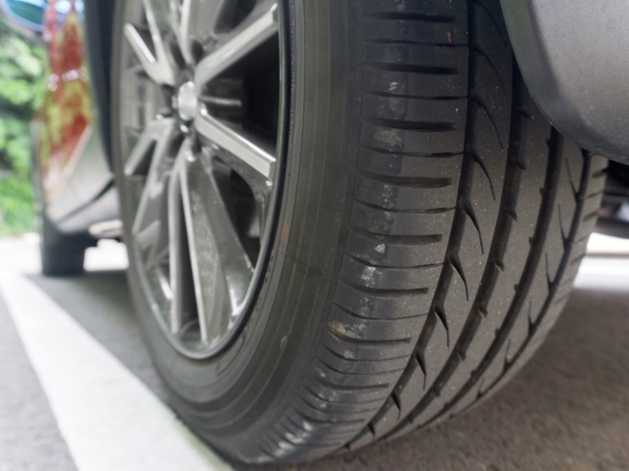 Nahaufnahme eines Autoreifens mit schwarzer Felge. Das Profil des Reifens ist deutlich sichtbar und zeigt ein Muster aus Rillen und Einschnitten für Fahrbahnhaftung.