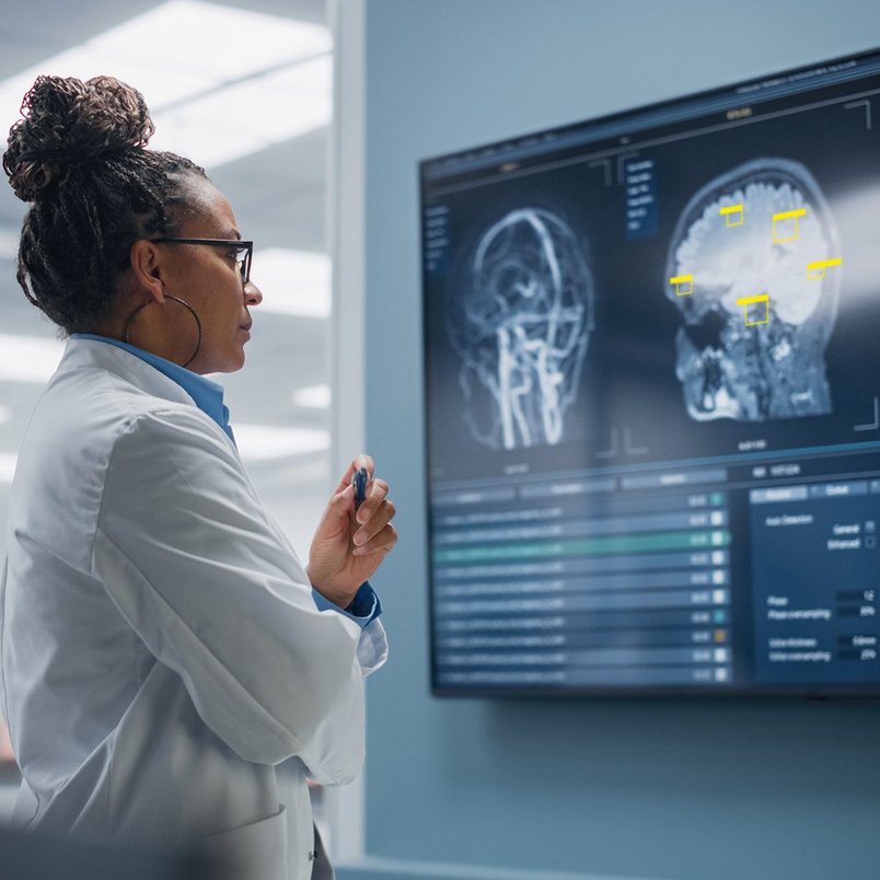 Eine Medizinerin steht vor einem Bildschirm, auf dem bildgebende KI einen medizinischen Scan auswertet. 