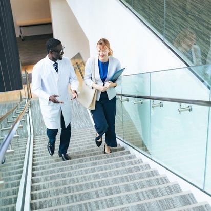 A doctor and a counselor walk up a staircase while talking A doctor and a counselor walk up a staircase while talking