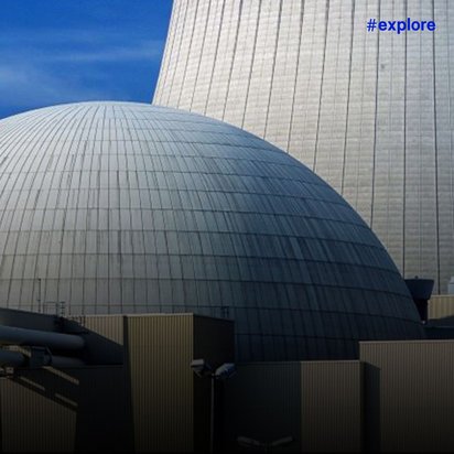 Kernkraftwerk mit charakteristischer Kuppel (Reaktorgebäude) und Kühltürmen vor blauem Himmel.