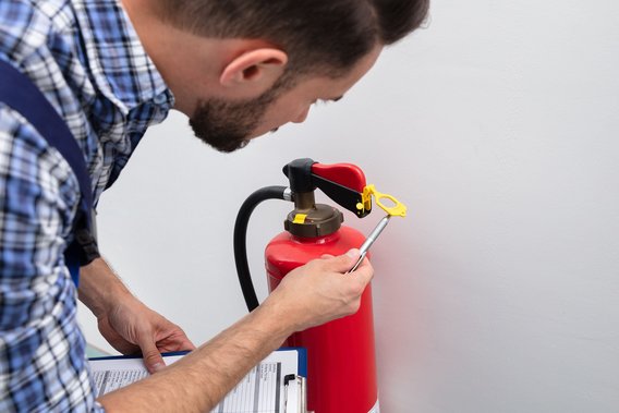 Mann kontrolliert einen Feuerlöscher und notiert die Ergebnisse auf einem Klemmbrett