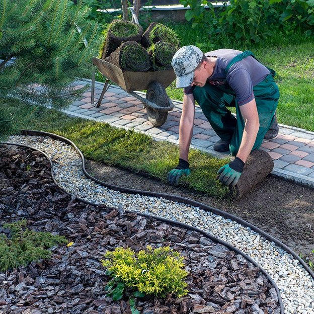 Gärtner verlegt Rollrasen in einem sorgfältig gestalteten Gartenbereich