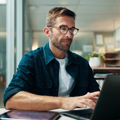 Ein Datenschutzauditor sitzt am Schreibtisch und arbeitet konzentriert an einem Laptop in einer modernen Büroumgebung.